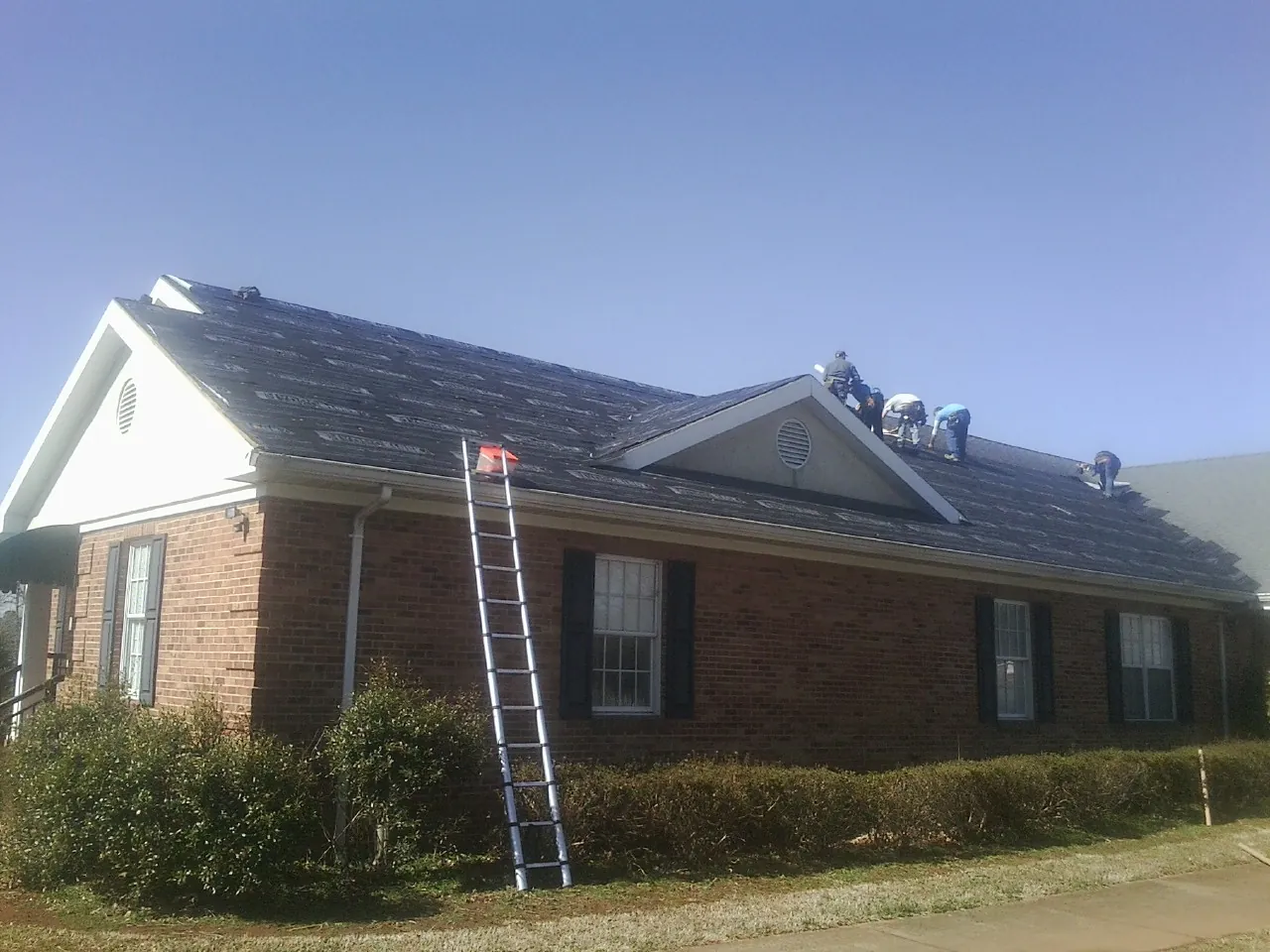 Crew tearing shingles off a brick ranch roof with a ladder set — Metal Roof Repair work by our crew in West Bridgewater