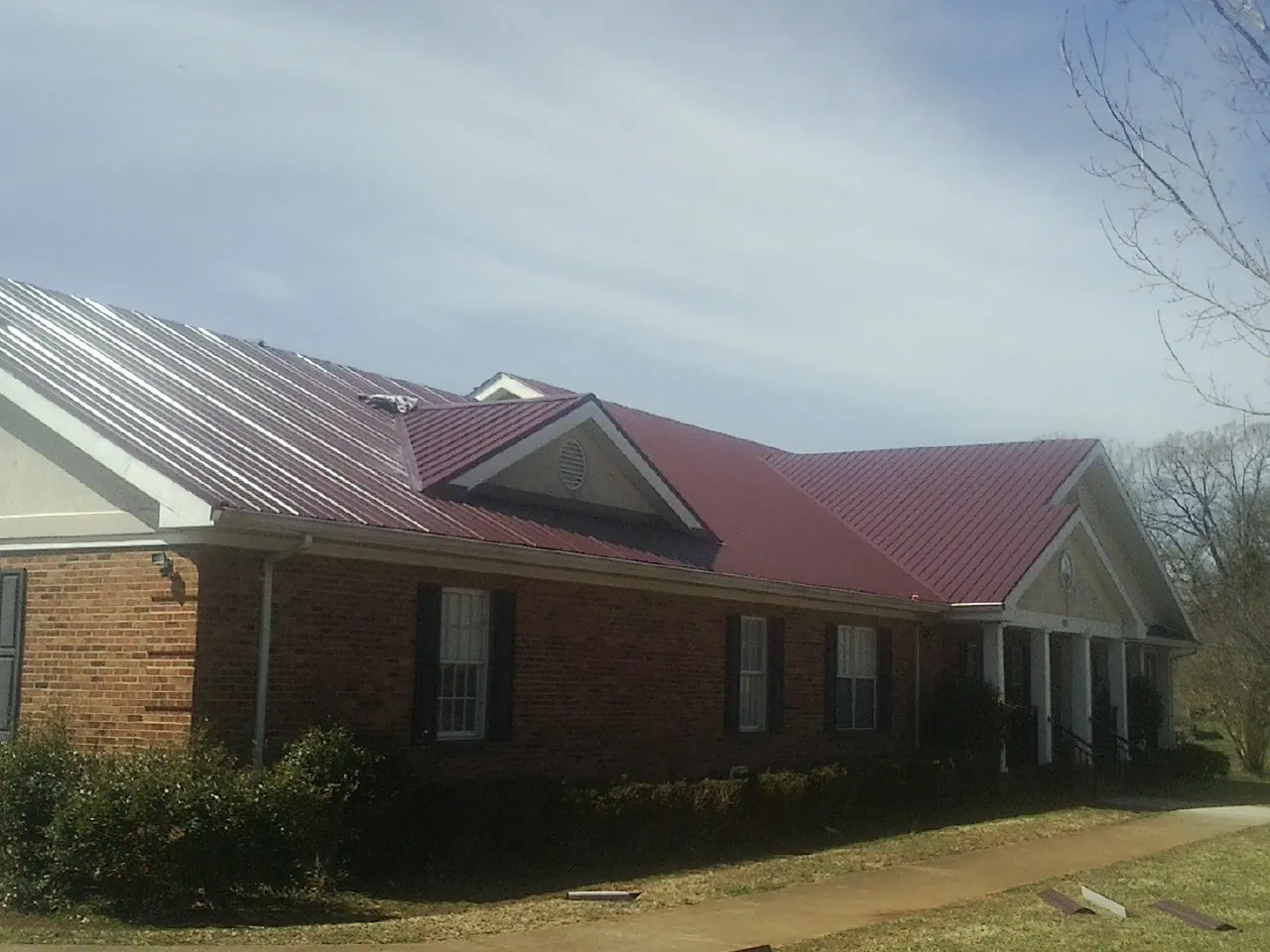 Red metal roof with gabled entries on a long brick building, from a Hail Damage Roof Repair job in West Bridgewater