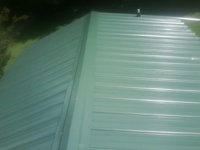 New green metal panels meeting at the ridge of a roof — Flat Roof Repair work by our crew in West Bridgewater
