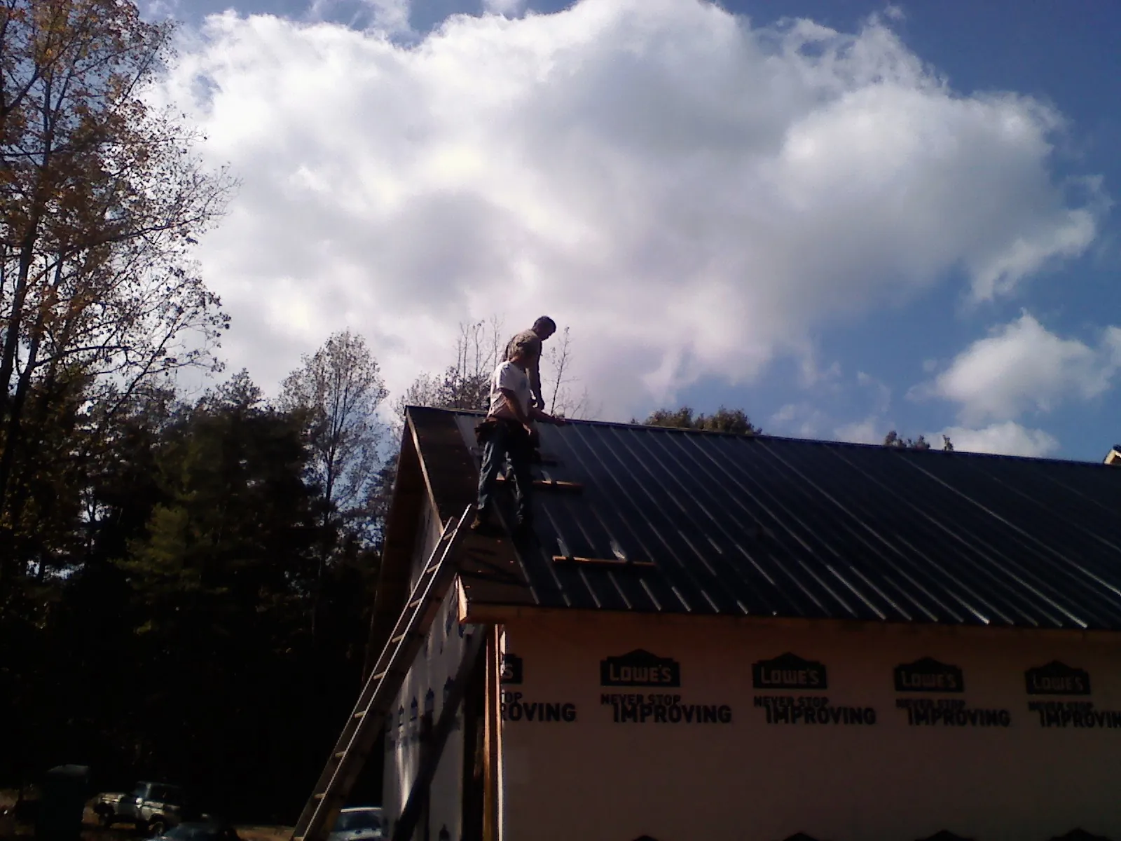 Roofer fastening dark metal panels high against a cloudy sky, from a Roof Inspection job in West Bridgewater