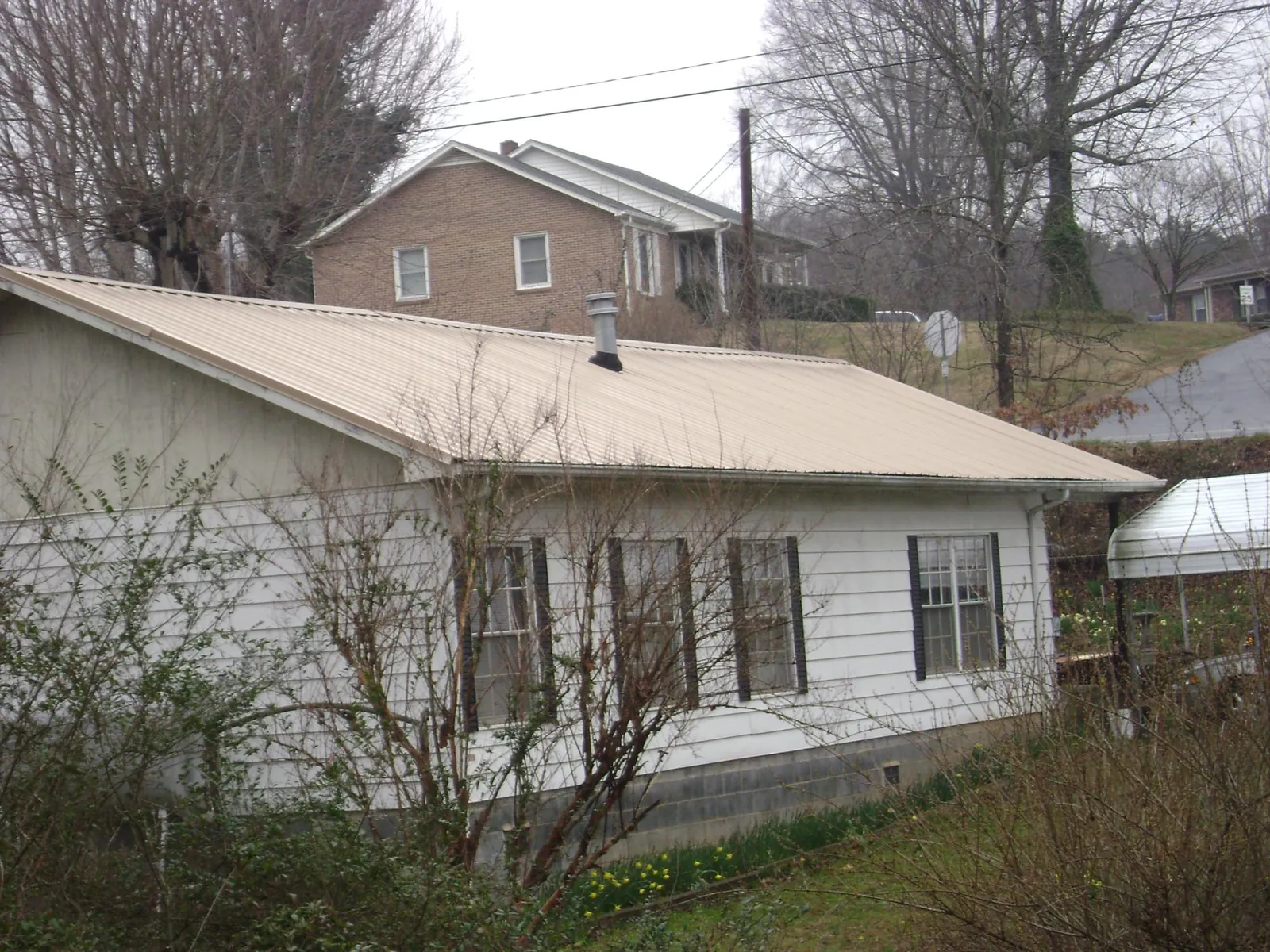 Tan metal roof on a white sided house set into a hillside — Commercial Roofing by Roofing Brothers in West Bridgewater